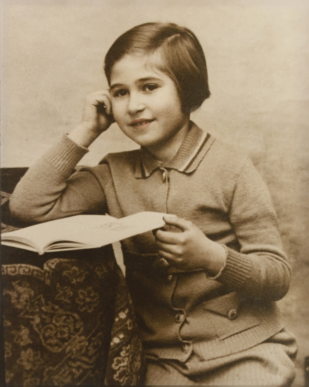 Photo de couleur sépia d'une jeune fille assise à une table sur laquelle il y a une nappe. La fille retient un livre ouvert sur la table d'une main et s'appuie sur l'autre d'une manière pensive. Un léger ton de rose a été ajouté à ses lèvres.
