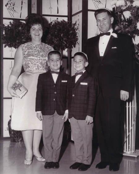 Black-and-white photograph of a man and woman with their two young sons. The family is formally dressed, the man and boys wearing suits with bowties, and the woman wears a dress.