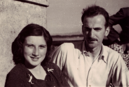Photo en noir et blanc d'un homme et d'une femme, assis ensemble à l'extérieur. La femme a de cheveux bruns jusqu'aux épaules et l'homme porte une moustache ainsi qu'une chemise à col de couleur pâle.