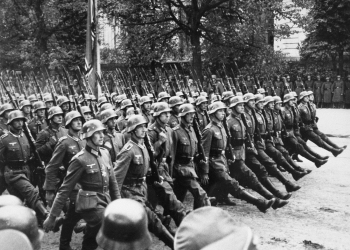 Black-and-white photograph of a large group of soldiers marching in unison on a boulevard.