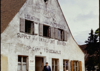 Colour slide of the exterior view of a three-storey building. Three men stand outside the building.