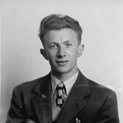 Black-and-white square-shaped identity photograph of a young man, wearing a suit, and smiling at the camera.