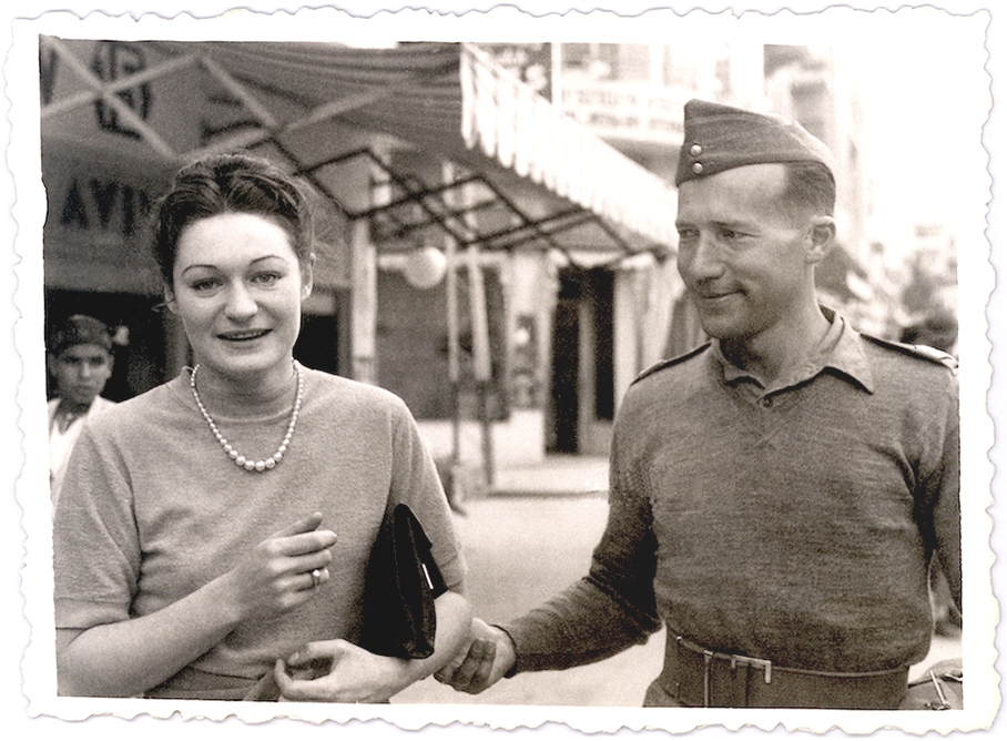 Photo en noir et blanc d'une femme et d'un homme à l'extérieur. La femme tient une petite bourse sous son bras et fait face à la caméra en souriant. L'homme regarde la femme et lui tient le coude.