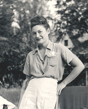 Black and white photo of a woman standing in a garden. She wears shorts and summer clothes.