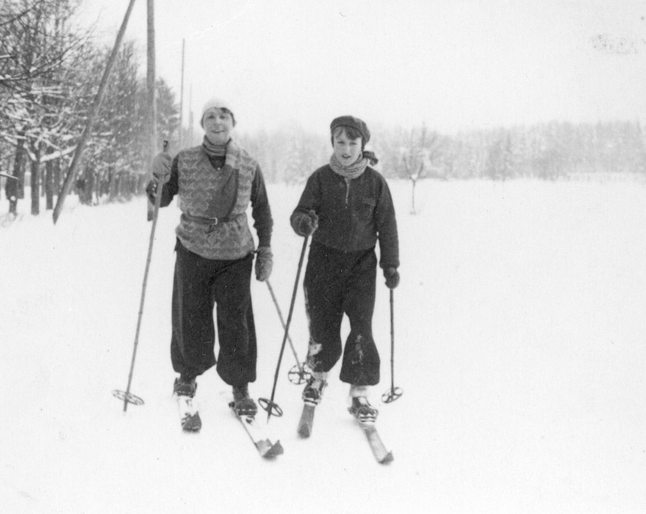 Photo en noir et blanc d'une femme et d'un jeune garçon portant des vêtements d'hiver et faisant du ski de fond sur un terrain enneigé.