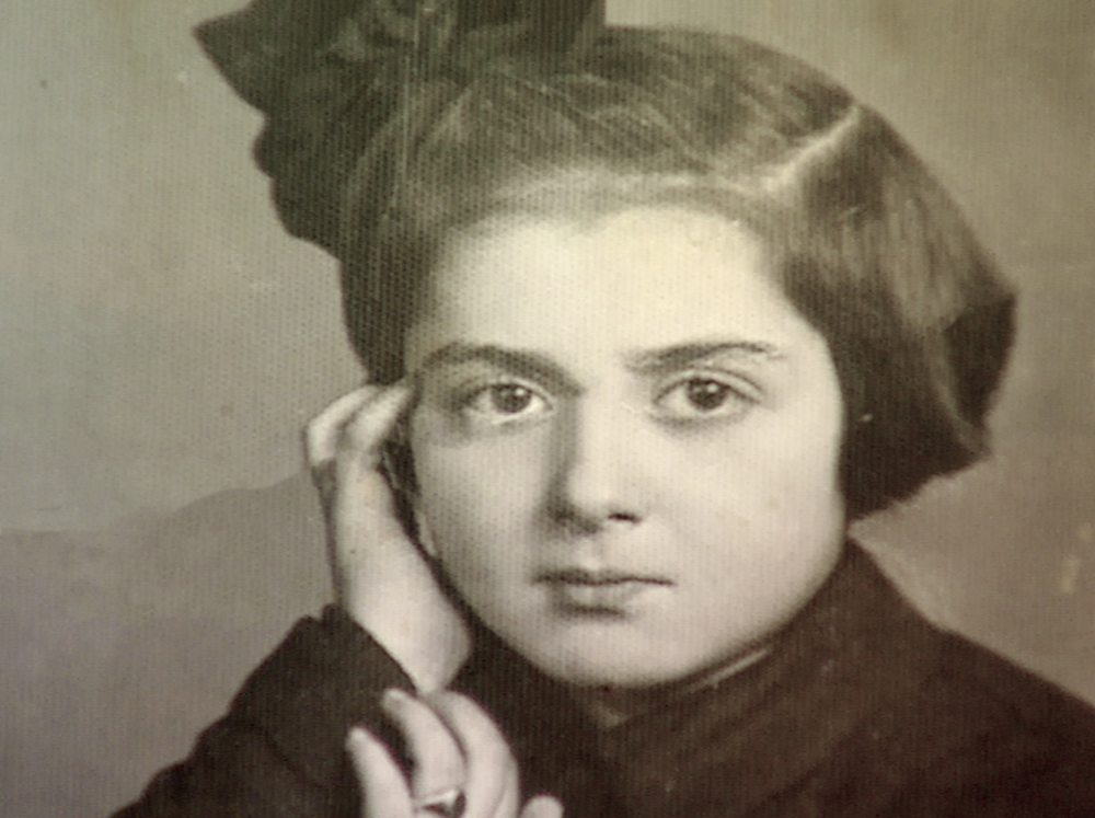 Black-and-white portrait photograph of a young girl looking at the camera. She rests her head against her hand, and wears a bow in her short, dark brown hair.