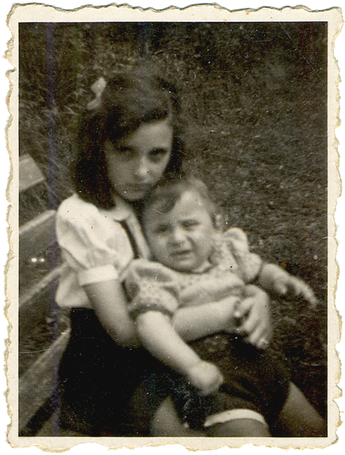 Black-and-white photograph of a girl sitting on a bench, holding a young toddler on her lap. The girl has a bow in her hair. The two siblings look at the camera, neither of them smiling.