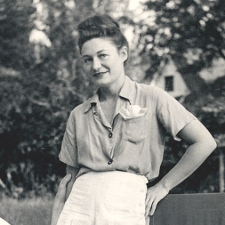Black and white photo of a woman standing in a garden. She wears shorts and summer clothes.