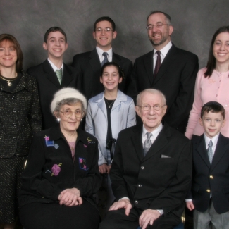 Colour studio photograph of nine people grouped together as a family in two rows, smiling at the camera.