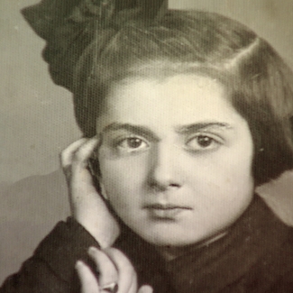 Black-and-white portrait photograph of a young girl looking at the camera. She rests her head against her hand, and wears a bow in her short, dark brown hair.