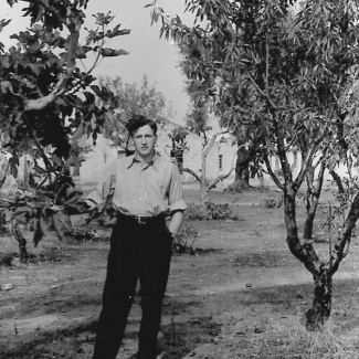 Photo en noir et blanc d'un jeune homme se tenant debout sur une pelouse, avec un arbre de chaque côté de lui.