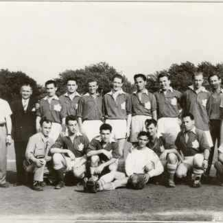 Black-and-white photograph of a soccer team of about 15 young men and 4 coaches, posing in two rows on a soccer field. Their soccer uniforms feature a Canadian flag on their chest.