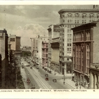 Black-and-white photograph with lightly coloured buildings in yellow and pink, depicting the view of a city street with brick buildings and storefronts. There are signs on three buildings for The McIntyre Block, Marathon Blue Gas, and Bank of Montreal