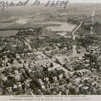 Photo aérienne en noir et blanc d'une ville où une rivière peut être aperçue au loin. Un texte est manuscrit dans le coin supérieur gauche de la photo.