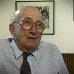 Screenshot of Holocaust survivor Gerhart Maass video testimony. He is sitting in front of a wall with three paintings, and looking to the right of the camera. The camera shows his face and shoulders.