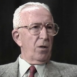 Screenshot of Holocaust survivor Jack Hahn video testimony. He is sitting in front of a dark background, and looking to the right of the camera. The camera shows his face and shoulders.