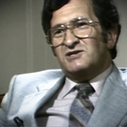 Screenshot of Holocaust survivor David Mark testimony video. He is sitting in front of a grey background, and looking to the left of the camera. The camera shows his face and shoulders.