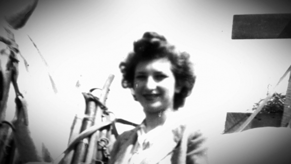 Black-and-white photograph of a woman smiling at the camera, standing beside a white horse with her hand resting on the horse’s reigns.