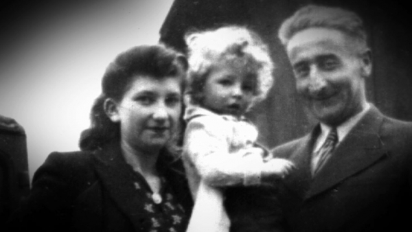 Photo en noir et blanc d’une femme, Minna Loewith, debout à côté un homme qui tient dans ses bras un garçon avec des cheveux blonds bouclés.