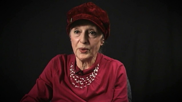 Capture d'écran du témoignage vidéo de  la survivante de l’Holocauste Sarah Engelhard, assise devant un fond noir, et regardant à la gauche de la caméra. Son visage et ses épaules sont visibles à la caméra.
