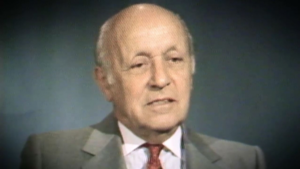 Capture d'écran du témoignage vidéo du survivant de l’Holocauste George Lysy, assis devant un fond gris, et regardant à la gauche de la caméra. Son visage et ses épaules sont visibles à la caméra.