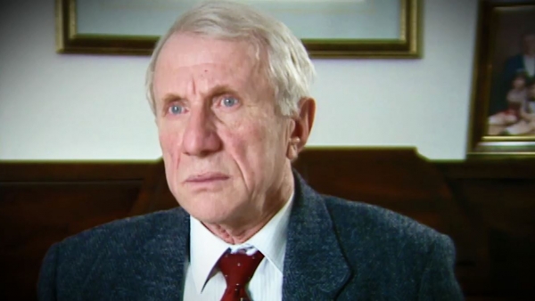 Screenshot of Holocaust survivor Elliott Zuckier video testimony, sitting in his living room, and looking to the left of the camera. The camera shows his face and shoulders.