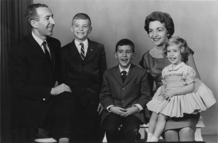 Photo en noir et blanc prise en studio d'un homme et d'une femme avec leur trois jeunes enfants, souriant à la caméra. L'homme et les deux garçons portent des complets, et la femme et sa fille portent des robes.