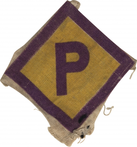 Colour photograph of a fabric badge in the shape of diamond. The centre is yellow with purple borders. In the middle of the badge is the capital letter ‘P’ in purple.