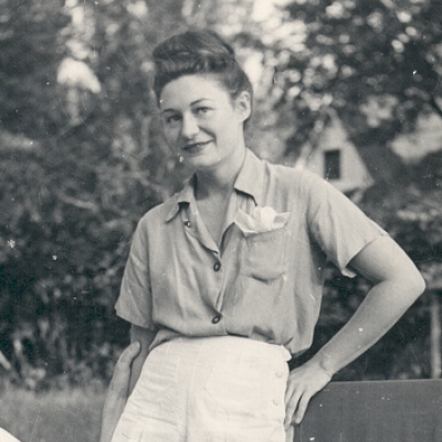 Photo en noir et blanc d'une femme debout dans un jardin. Elle porte des shorts et des vêtements estivaux.