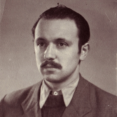 Photo de couleur sépia d'un homme, prise à partir de la potrine, regardant vers la gauche de la caméra. Il porte un complet et une cravate et ses cheveux sont coiffés vers l'arrière. Il porte une moustache.