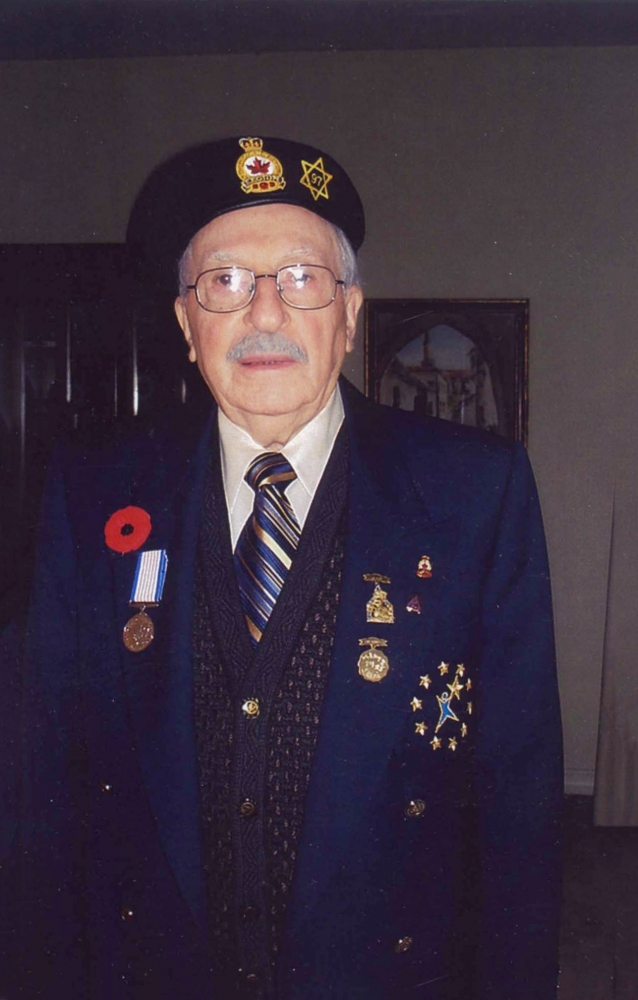 Colour photograph of an elderly man dressed in his military uniform, smiling at the camera. His jacket and beret are adorned with medals and pins, as well as a Remembrance Day poppy.