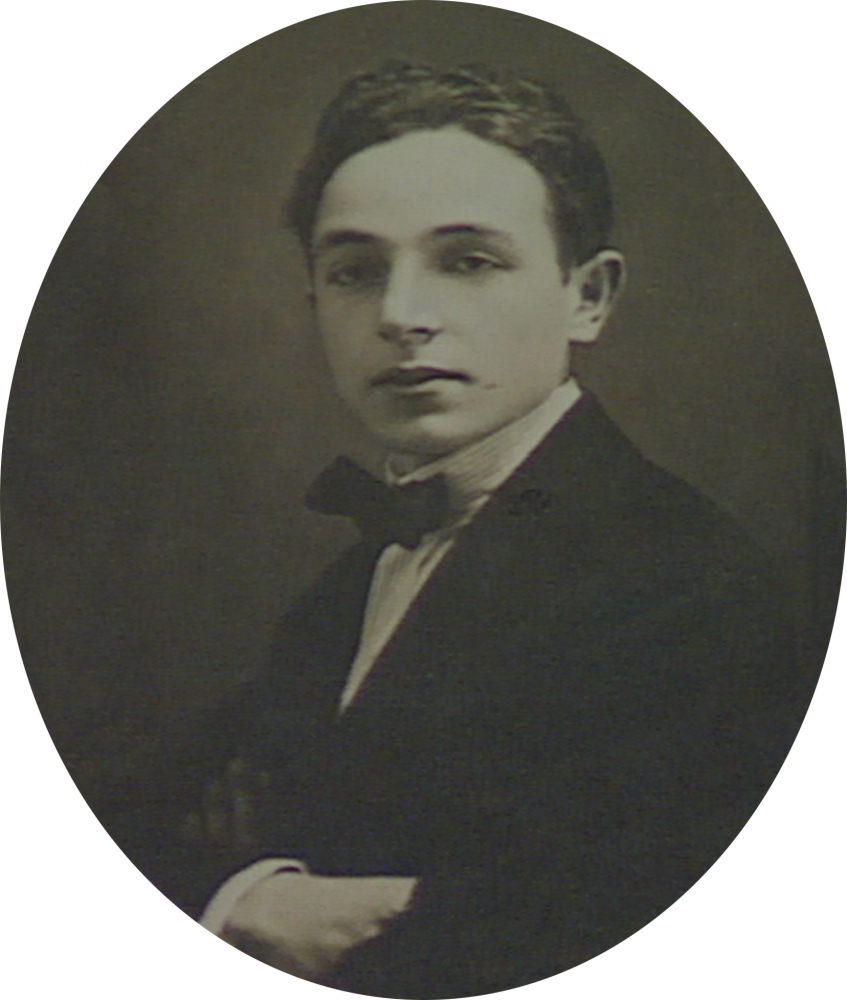 Photo en noir et blanc de forme ovale, prise en studio, d'un jeune homme. L'homme porte un complet avec un nœud papillon. La photo a une grande bordure blanche.