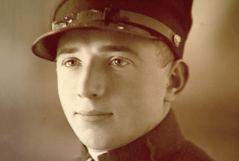 Sepia-toned photograph depicting the close-up of a man’s face. The man looks to the left of the camera, wearing what appears to be a military uniform.