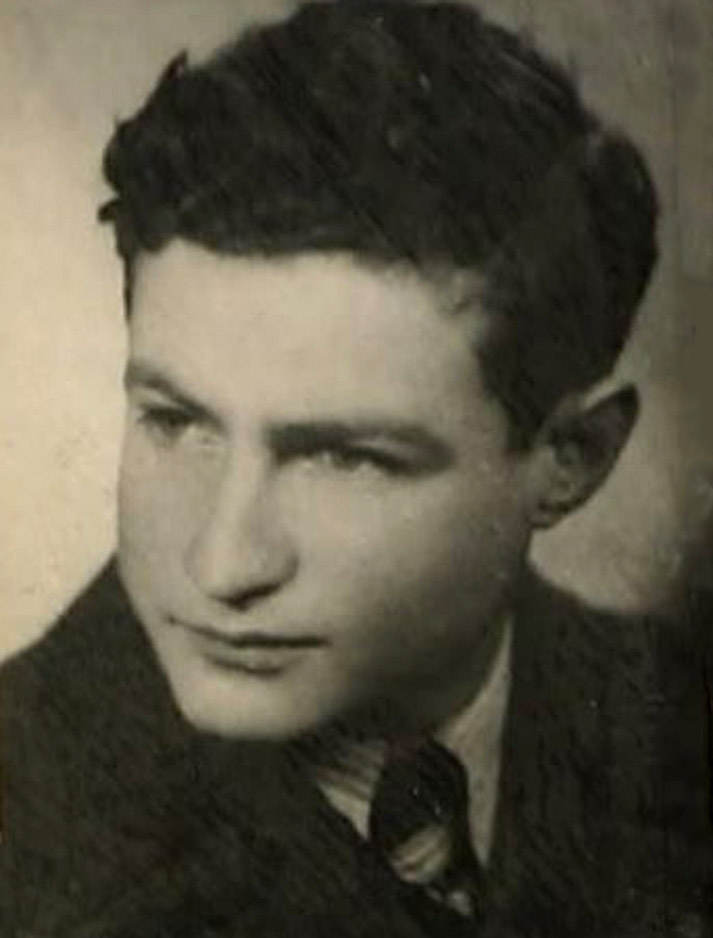 Photo en noir et blanc du profil d'un jeune homme, regardant vers la gauche de la caméra. il porte un complet et a des cheveux bruns foncés bouclés.