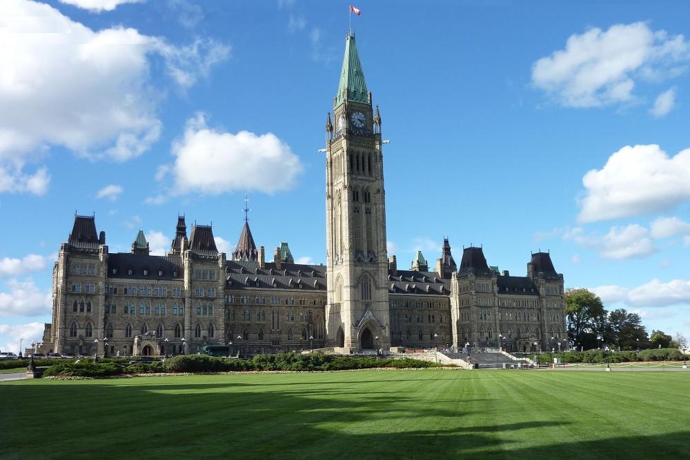 Color photo of the Canadian parliament central building with green grass at the front and a blue sky with a couple of clouds.