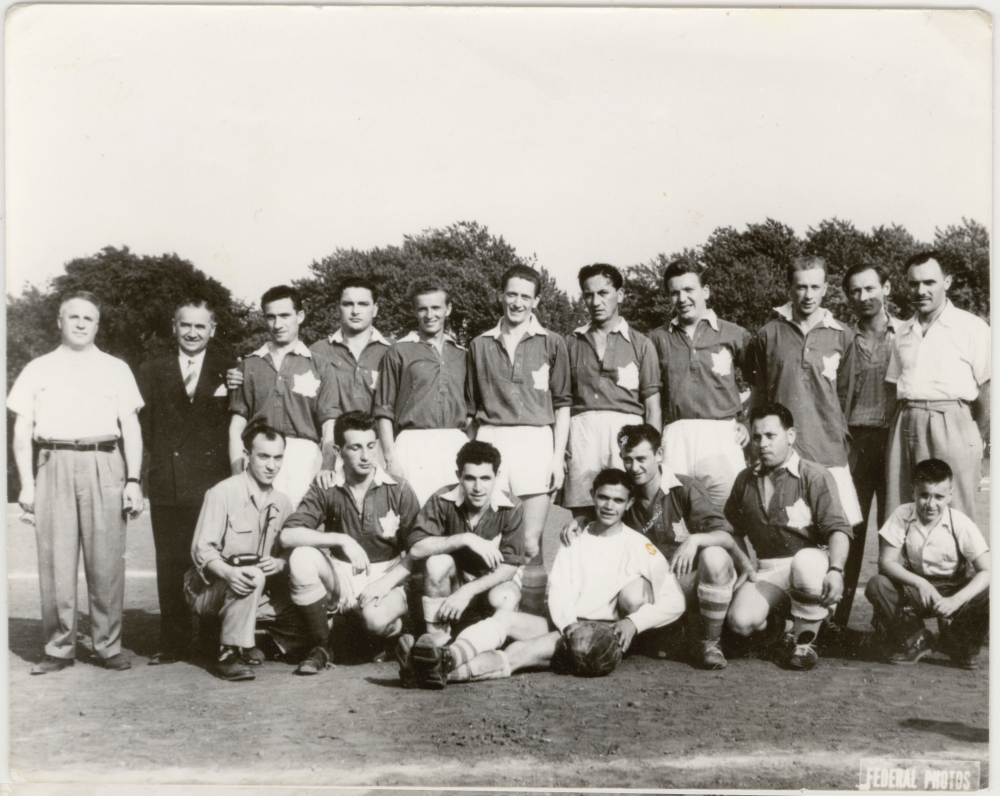 Black-and-white photograph of a soccer team of about 15 young men and 4 coaches, posing in two rows on a soccer field. Their soccer uniforms feature a Canadian flag on their chest.