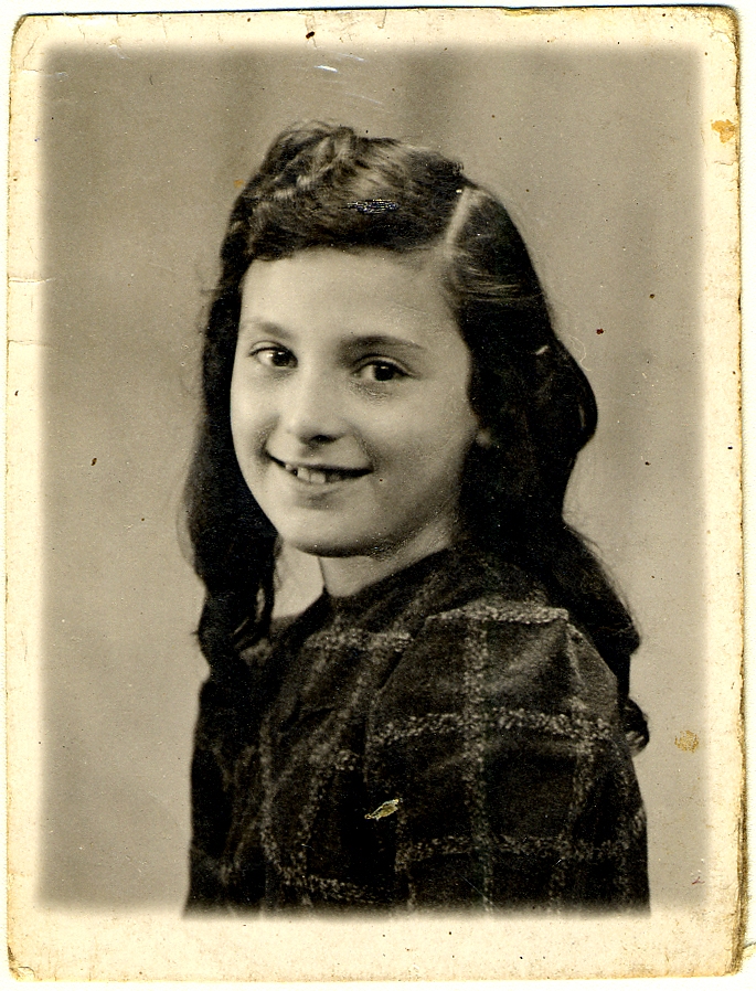 Portrait photographique en noir et blanc d'une jeune fille, la tête tournée et souriant vers la caméra. Elle a de longs cheveux bruns ondulés.