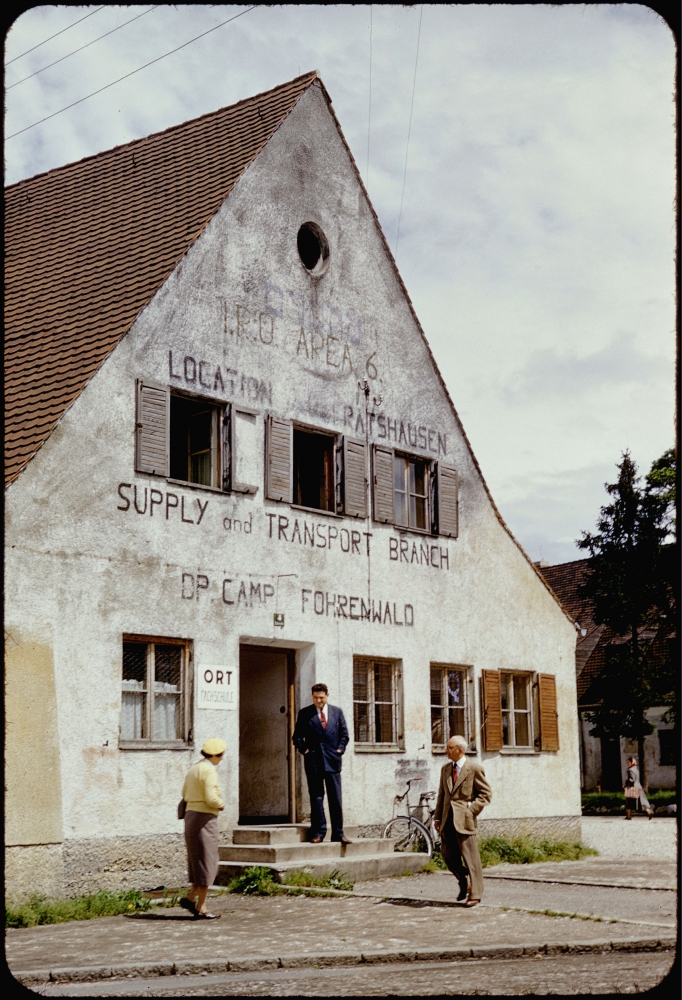 Colour slide of the exterior view of a three-storey building. Three men stand outside the building.