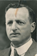 Portrait photographique en noir et blanc d'un homme, la photo est prise des épaules en montant. Il porte un veston et une cravate.