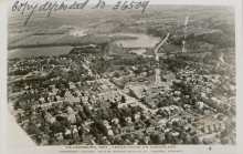 Photo aérienne en noir et blanc d'une ville où une rivière peut être aperçue au loin. Un texte est manuscrit dans le coin supérieur gauche de la photo.