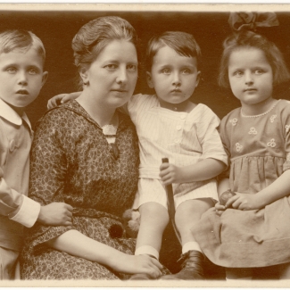 Portrait photographique de couleur sépia d'une femme avec trois jeunes enfants, posant ensemble  et étant habillés de manière formelle.