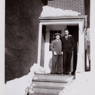 Photo en noir et blanc de deux hommes debout ensemble à l'extérieur d'un maison pendant l'hiver.