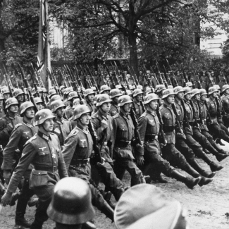 Photo en noir et blanc d'un grand groupe de soldats marchand au même rythme sur un boulevard.