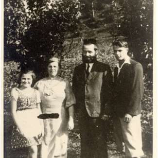 Black-and-white photograph of four people standing outdoors, with trees in the background.