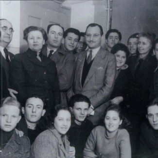 Photo en noir et blanc d'un grand groupe d'environ trente jeunes, rassemblés en deux rangées et souriant à la caméra. Un homme plus âgé portant un complet est debout au centre du groupe.