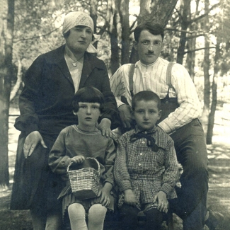 Photo en noir et blanc d'une famille de quatre, rassemblés ensemble pour une photo extérieure, entourés d'arbres. L'homme et la femme se tiennent derrière leur deux enfants assis.