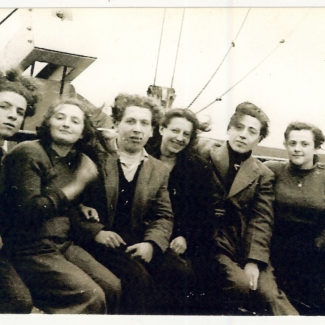 Black-and-white photograph of a group of 8 young adults, men and women, sitting together on the deck of a ship.