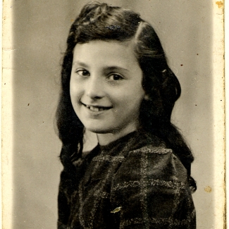 Black-and-white portrait photograph of a young girl, turning her head to smile at the camera. She has long, wavy brown hair.