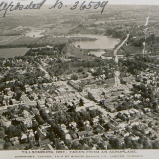 Black-and-white aerial photograph of a town with a river visible in the distance. Text has been handwritten in the top-left corner of the photograph.