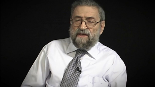 Capture d'écran du témoignage vidéo du survivant de l’Holocauste Joseph Lazar, assis devant un fond noir, et regardant à la gauche de la caméra. Son visage et ses épaules sont visibles à la caméra.
